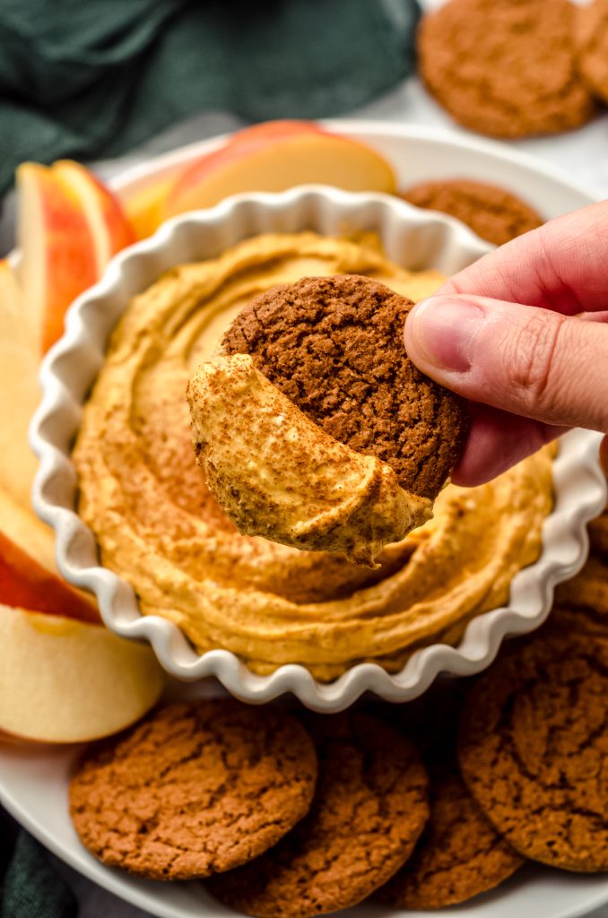 Someone is dipping a gingersnap into a bowl of pumpkin dip.