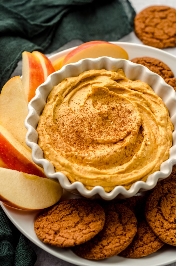 Pumpkin dip in a bowl on a plate with gingersnaps and apple slices.