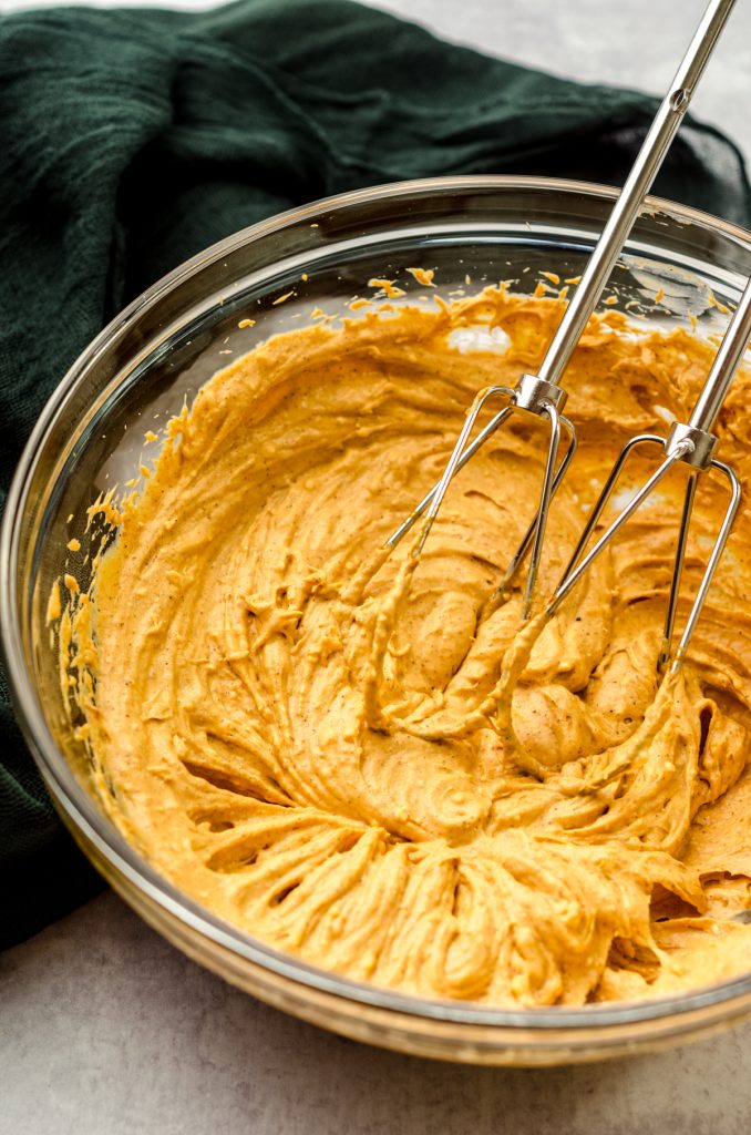 Pumpkin dip in a large glass bowl with beaters.