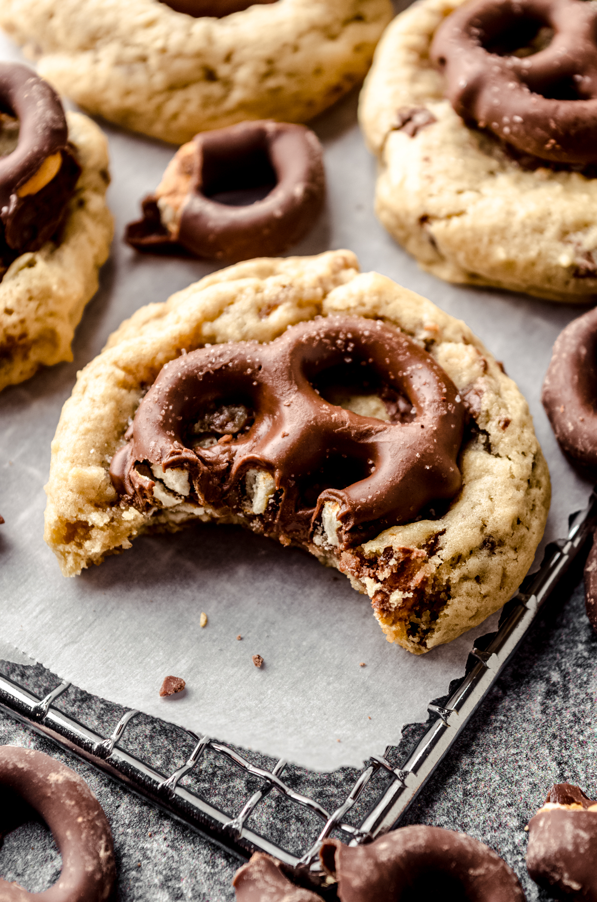 A photo of a chocolate covered pretzel with a bite taken out of it on a cooling rack and a piece of parchment.