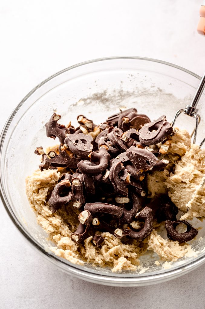 Chocolate covered pretzel cookie dough in a large glass bowl with a spatula.