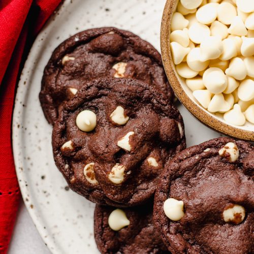 aerial photo of chocolate white chocolate chip cookies on a plate with a bowl of white chocolate chips