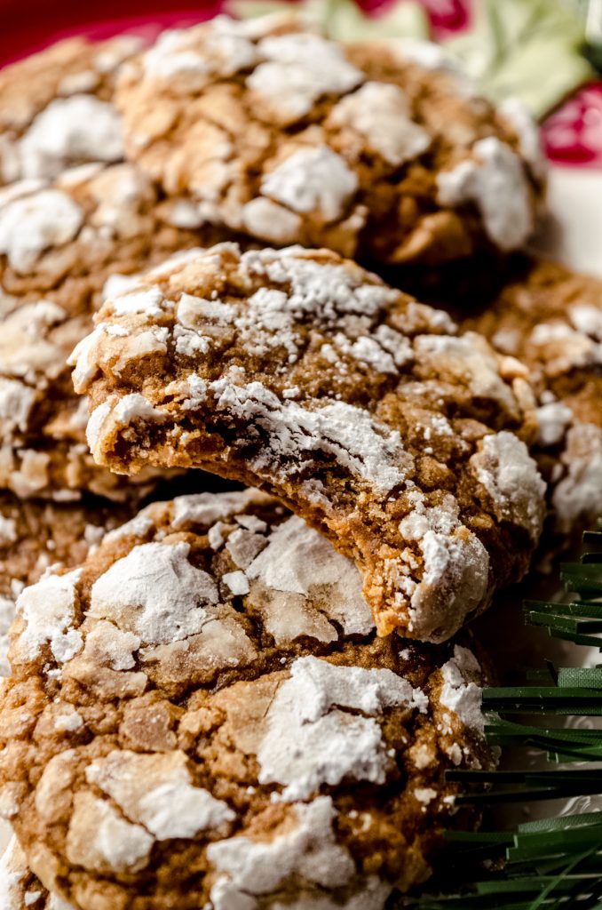 Gingerbread crinkle cookies in a pile and a bite has been taken out of the one on the top.