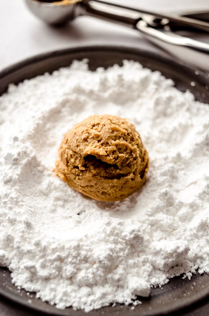 A ball of gingerbread crinkle cookie dough sitting in powdered sugar before rolling.