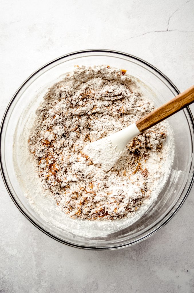 Gingerbread crinkle cookie dough coming together in a bowl with a spatula.