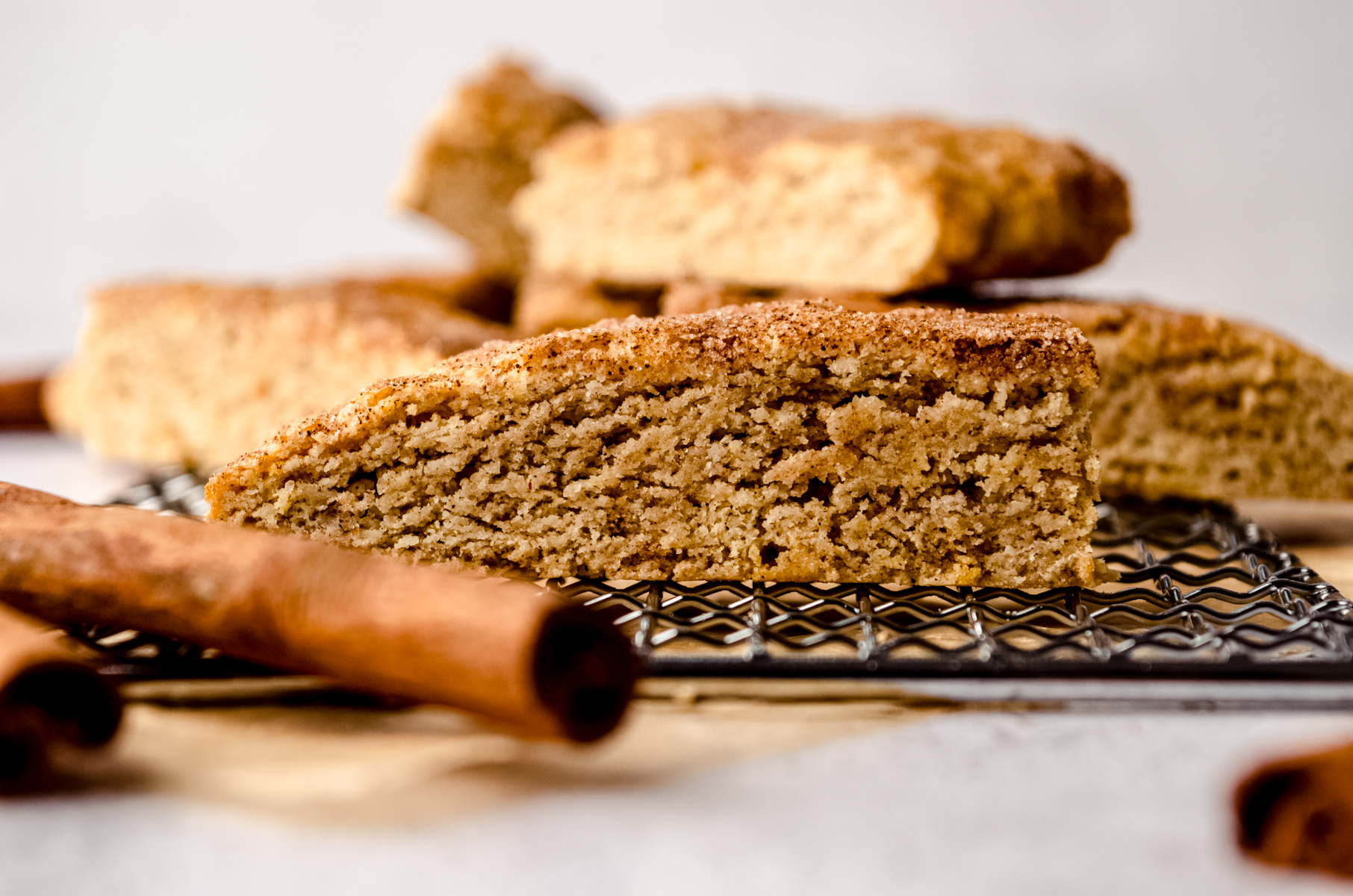 Snickerdoodle biscotti on a wire cooling rack with cinnamon sticks around it.