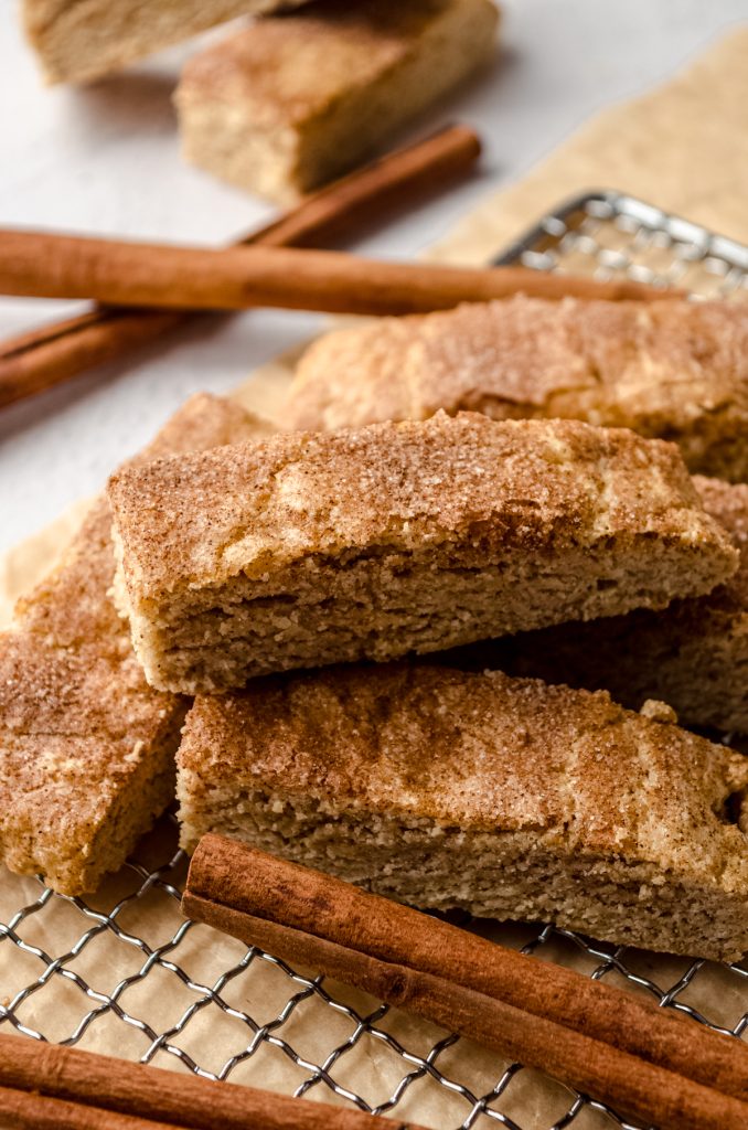 Snickerdoodle biscotti on a wire cooling rack with cinnamon sticks around it.