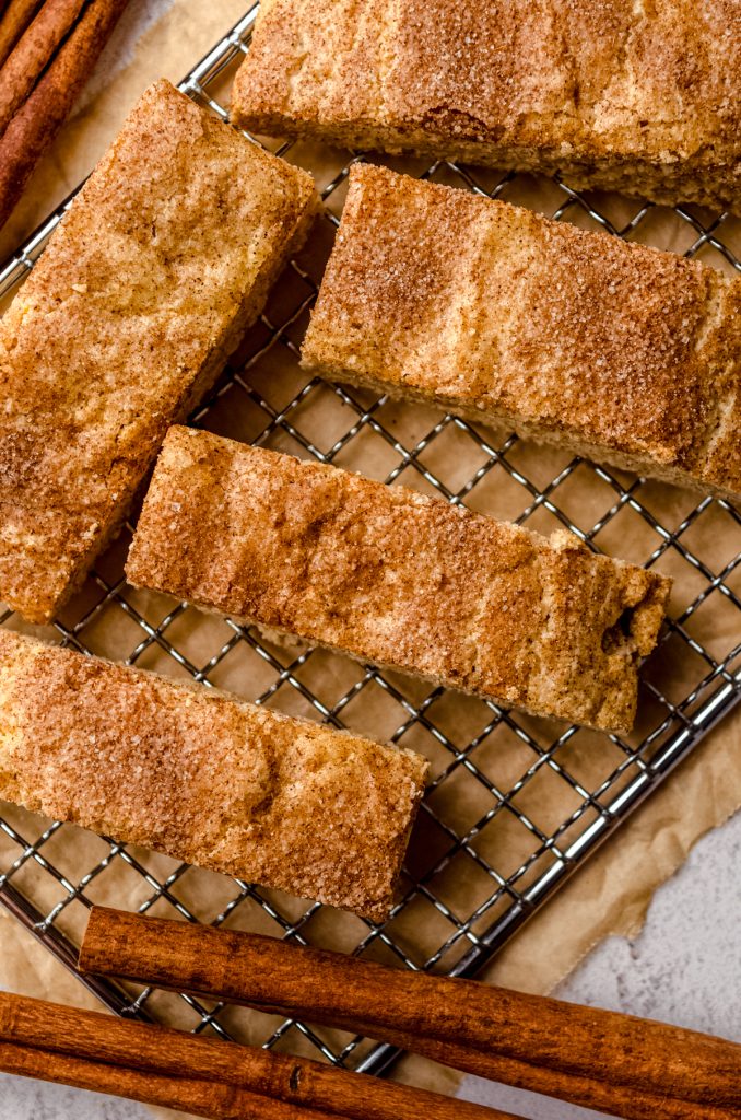 Aerial photo of snickerdoodle biscotti on a wire cooling rack with cinnamon sticks around it.