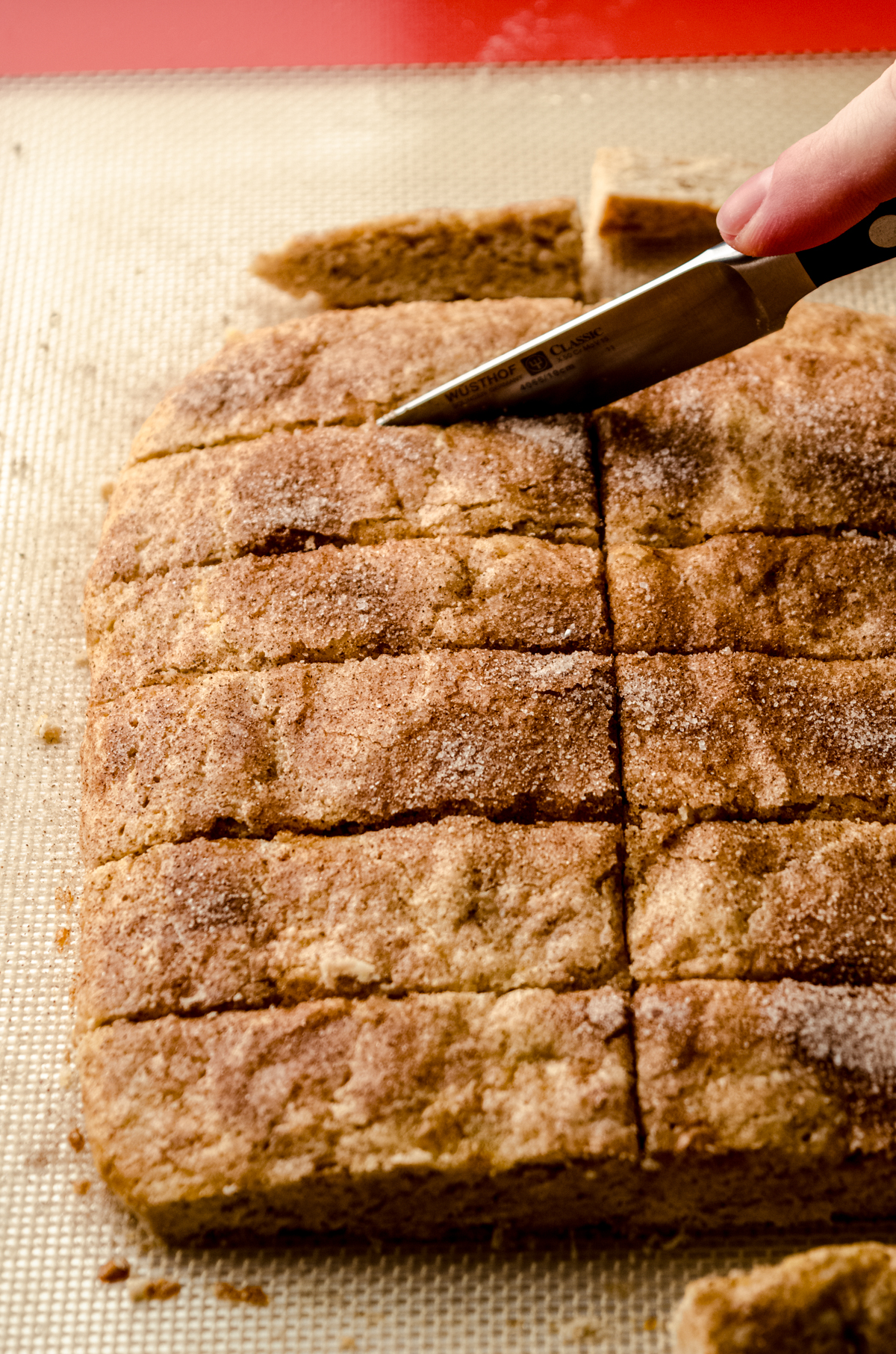 Someone is using a knife to cut a slab of biscotti into individual cookies.