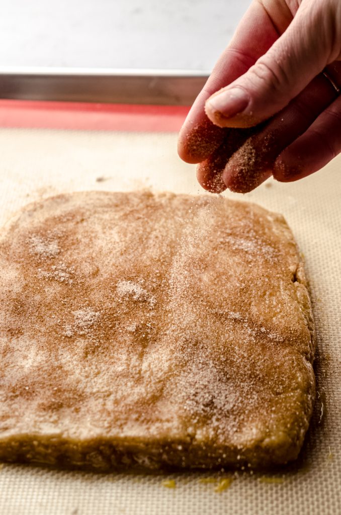 Someone is sprinkling a biscotti slab with a cinnamon sugar coating