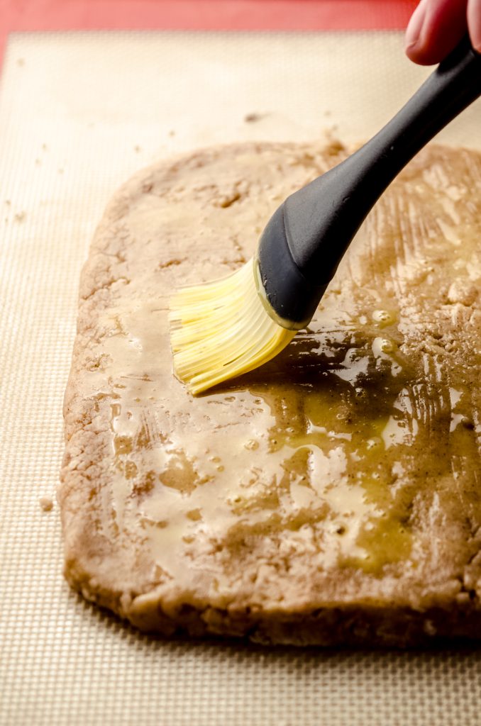 Someone is brushing a biscotti slab with an egg wash.