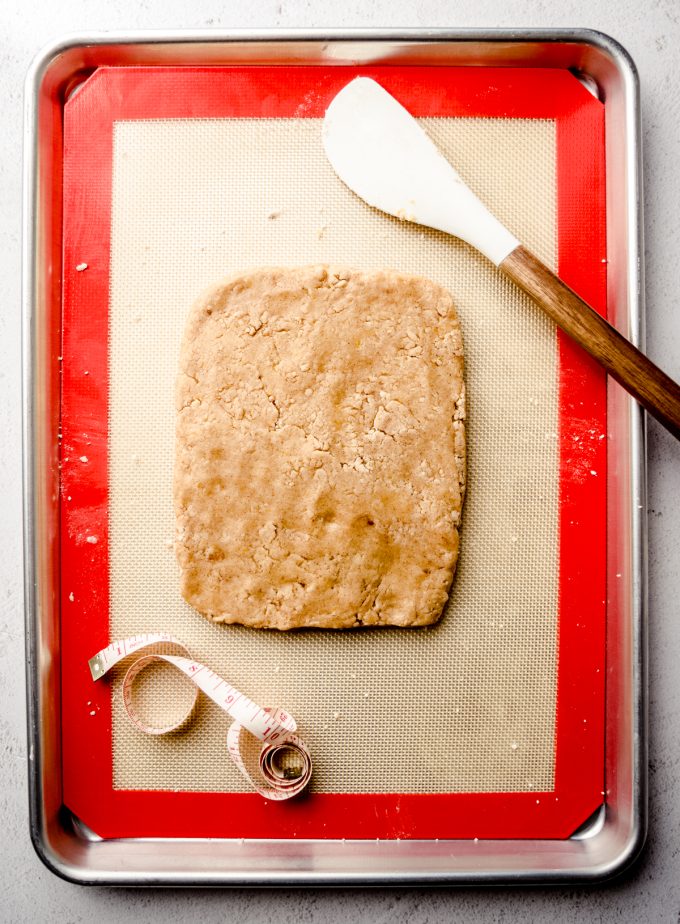 Aerial photo of the dough for biscotti pressed into a slab on a baking sheet with a spatula and a tape measure.