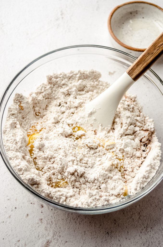 Dry ingredients and some wet ingredients in a bowl to make biscotti getting mixed together with a large spatula.