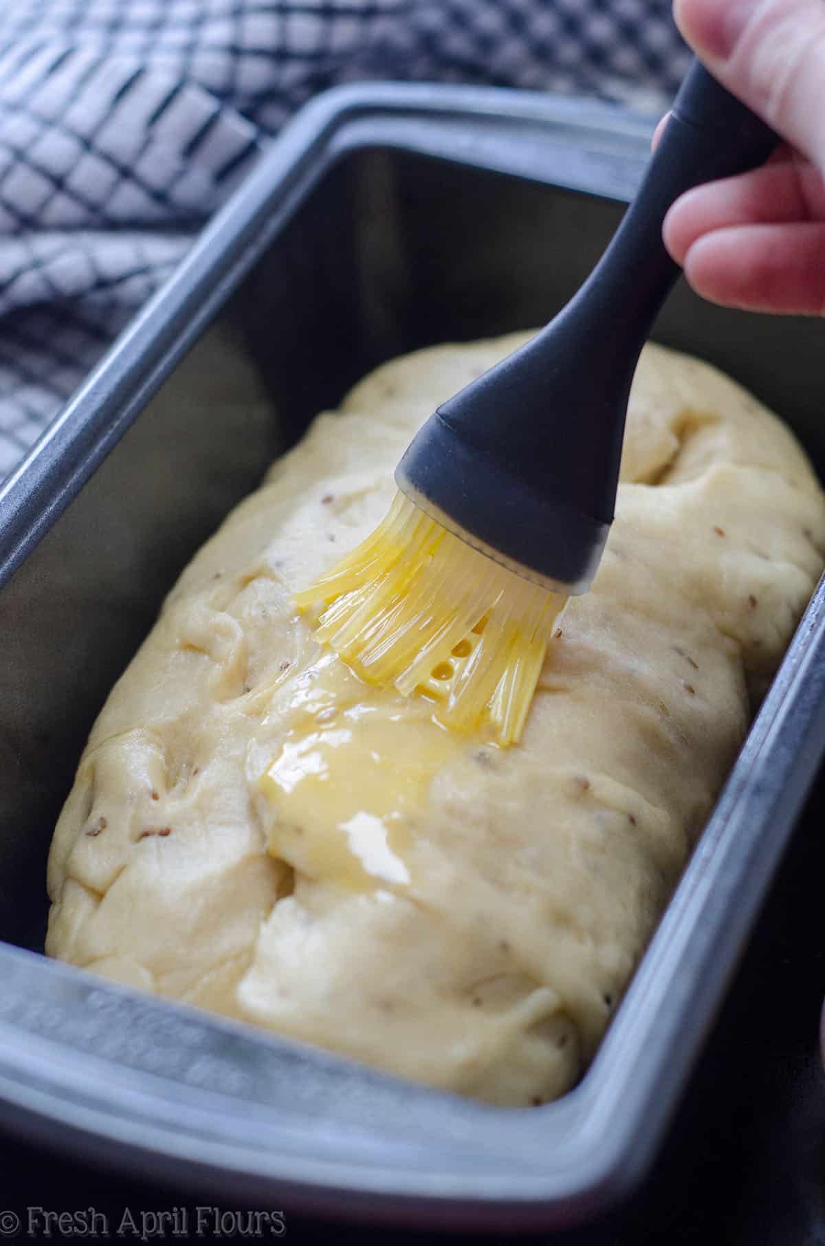 hand brushing an egg wash onto anise bread in a loaf pan