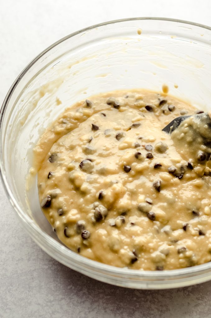Chocolate chip muffin batter in a glass bowl with a spatula.