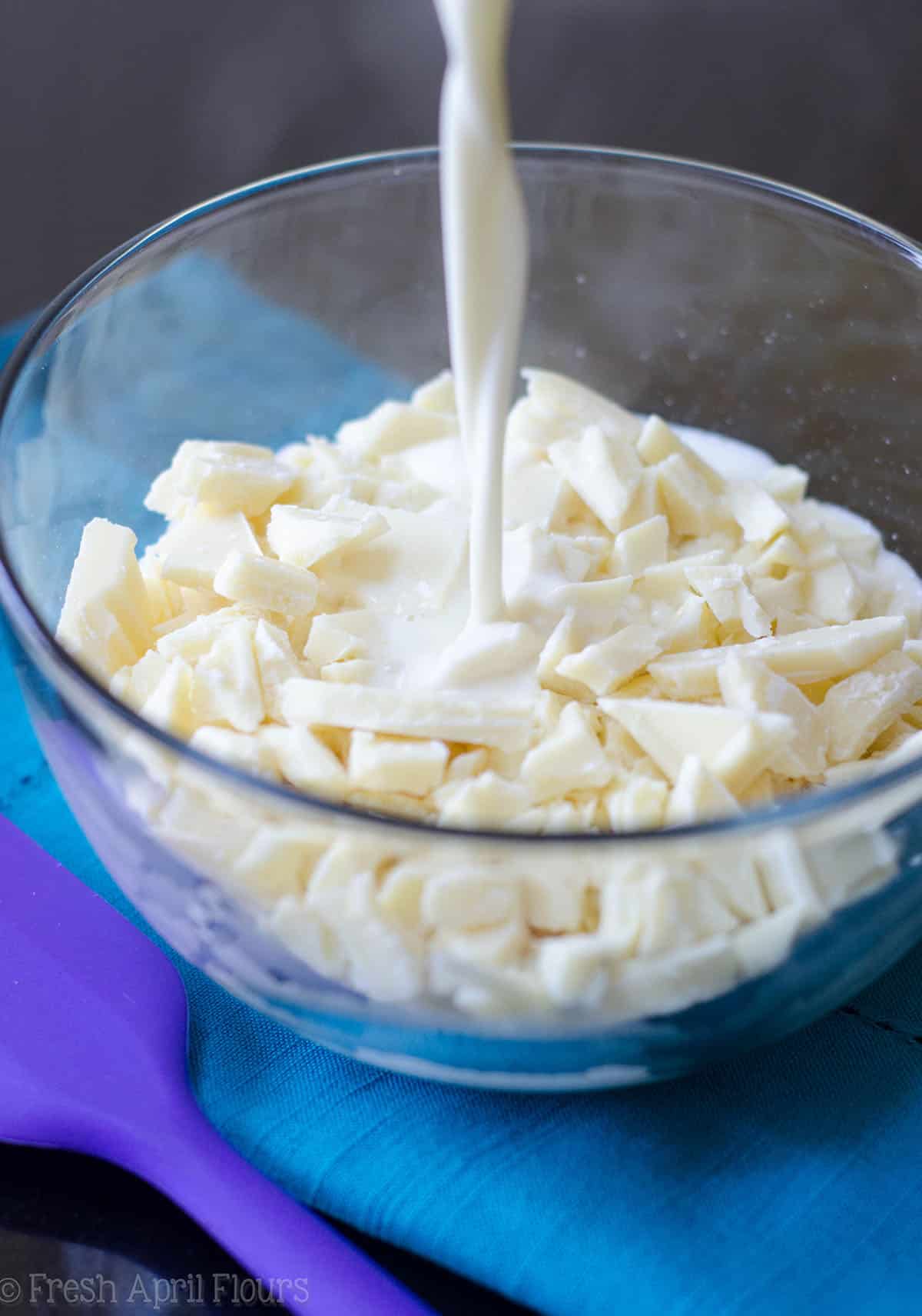 pouring warm cream onto chopped white chocolate in a bowl