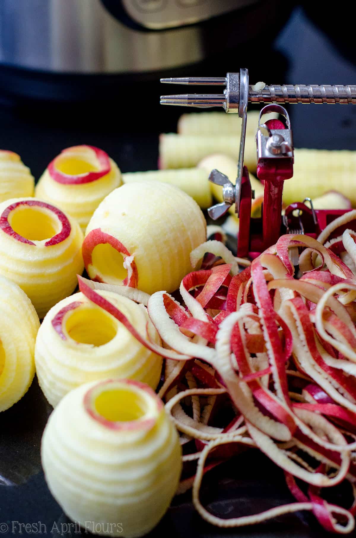 sliced and cored apples on a surface with an apple peeler in the background