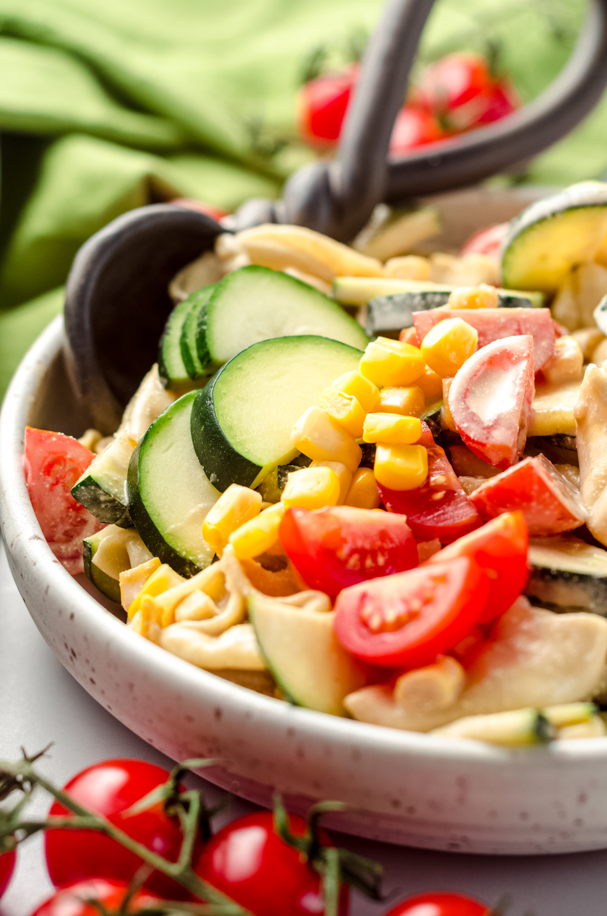 Tortellini pasta salad with zucchini, corn, and tomatoes in a bowl with a serving spoon.