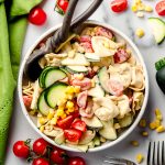 Tortellini pasta salad with zucchini, corn, and tomatoes in a bowl with a serving spoon.