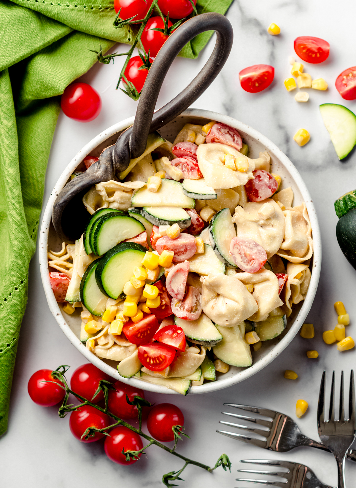 Tortellini pasta salad with zucchini, corn, and tomatoes in a bowl with a serving spoon.