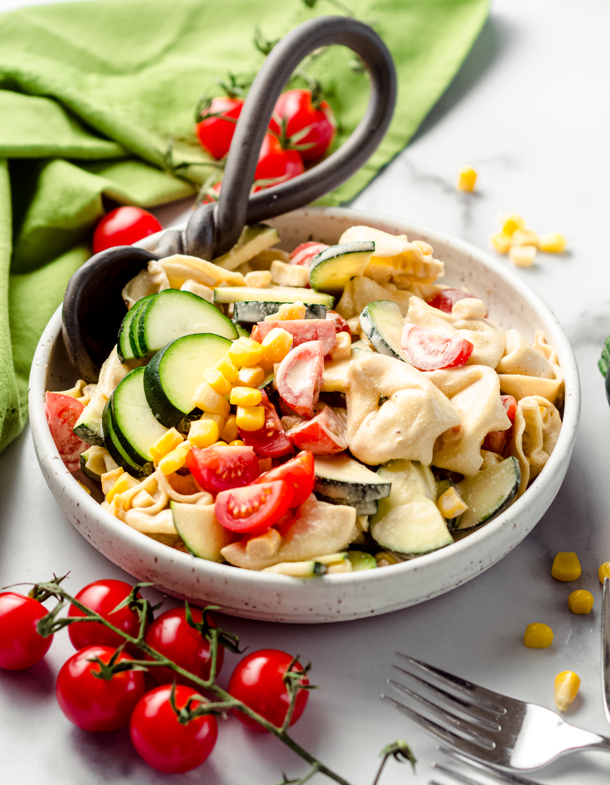 Tortellini pasta salad with zucchini, corn, and tomatoes in a bowl with a serving spoon.