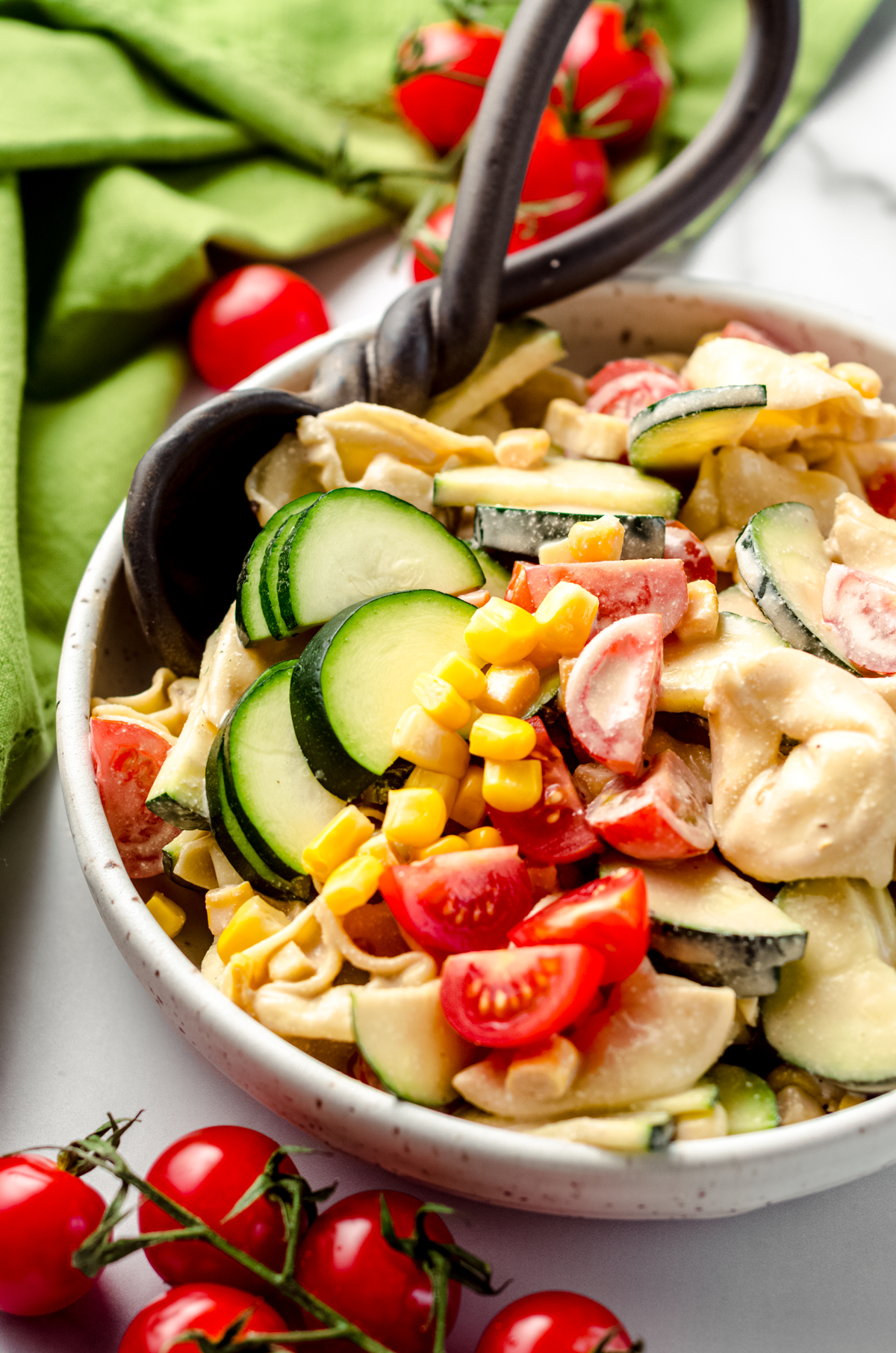 Tortellini pasta salad with zucchini, corn, and tomatoes in a bowl with a serving spoon.