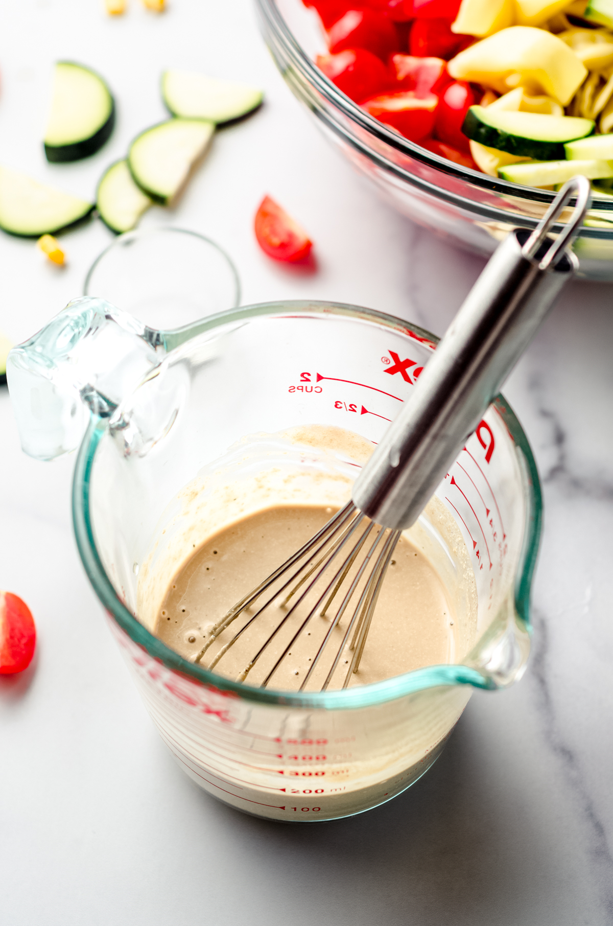 Dressing for tortellini summer pasta in a measuring cup with a whisk.