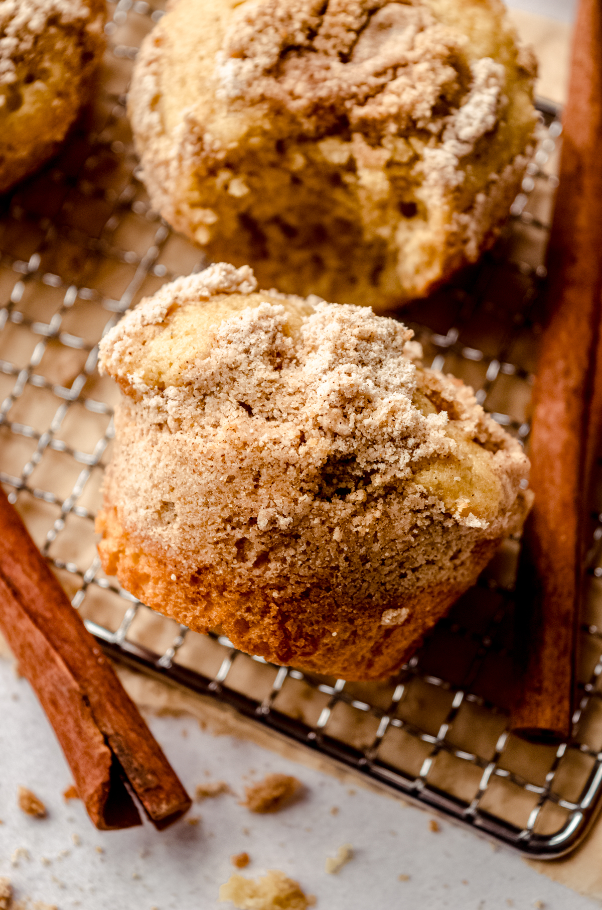 A coffee cake muffin on its side on a wire cooling rack with cinnamon sticks around it.