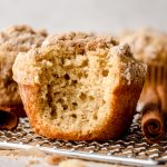 A coffee cake muffin with a bite taken out of it on a wire cooling rack.