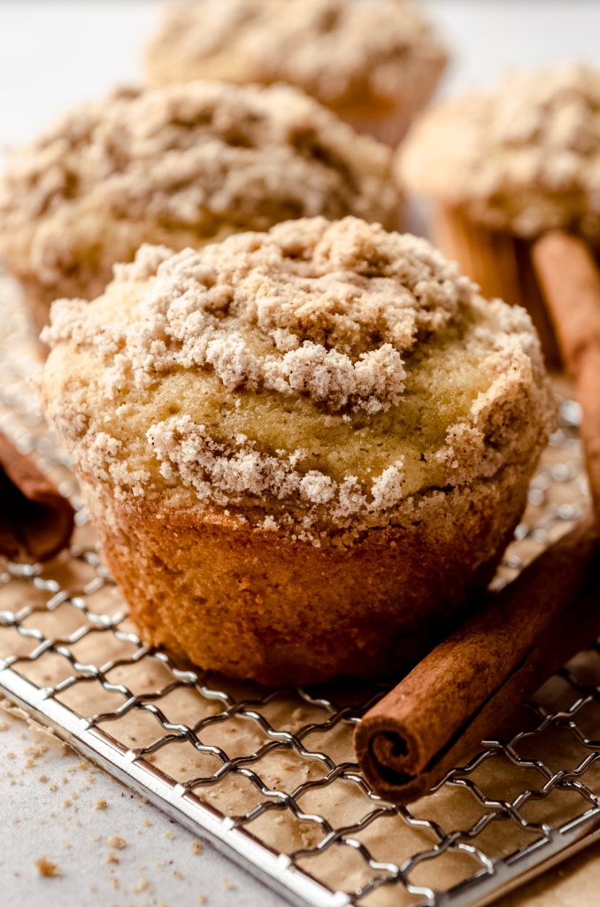 A coffee cake muffin on a wire cooling rack with cinnamon sticks around it.