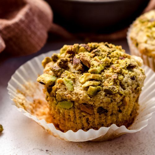 A pistachio muffin sitting in a wrapper.