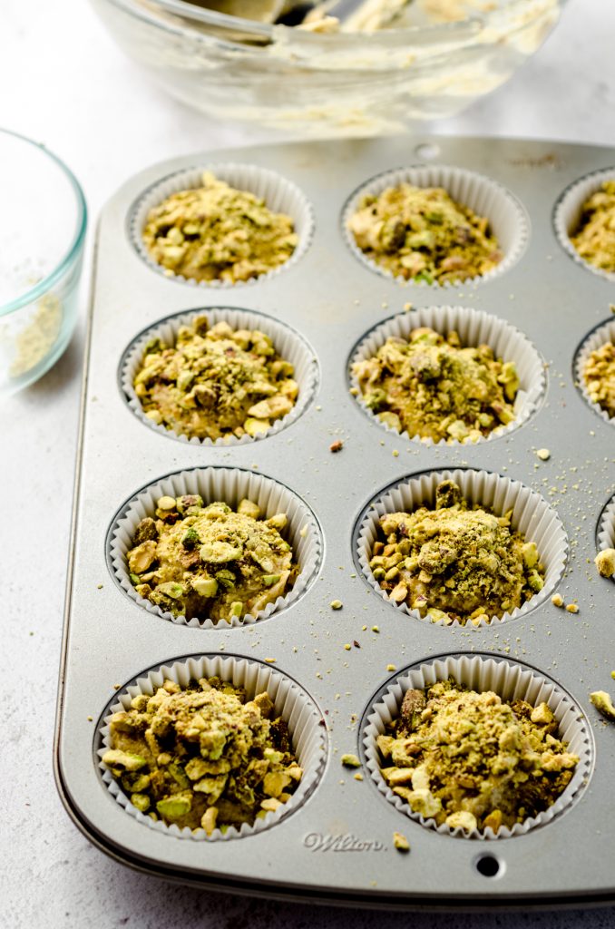 Pistachio muffin batter portioned out in a cupcake pan ready to bake.