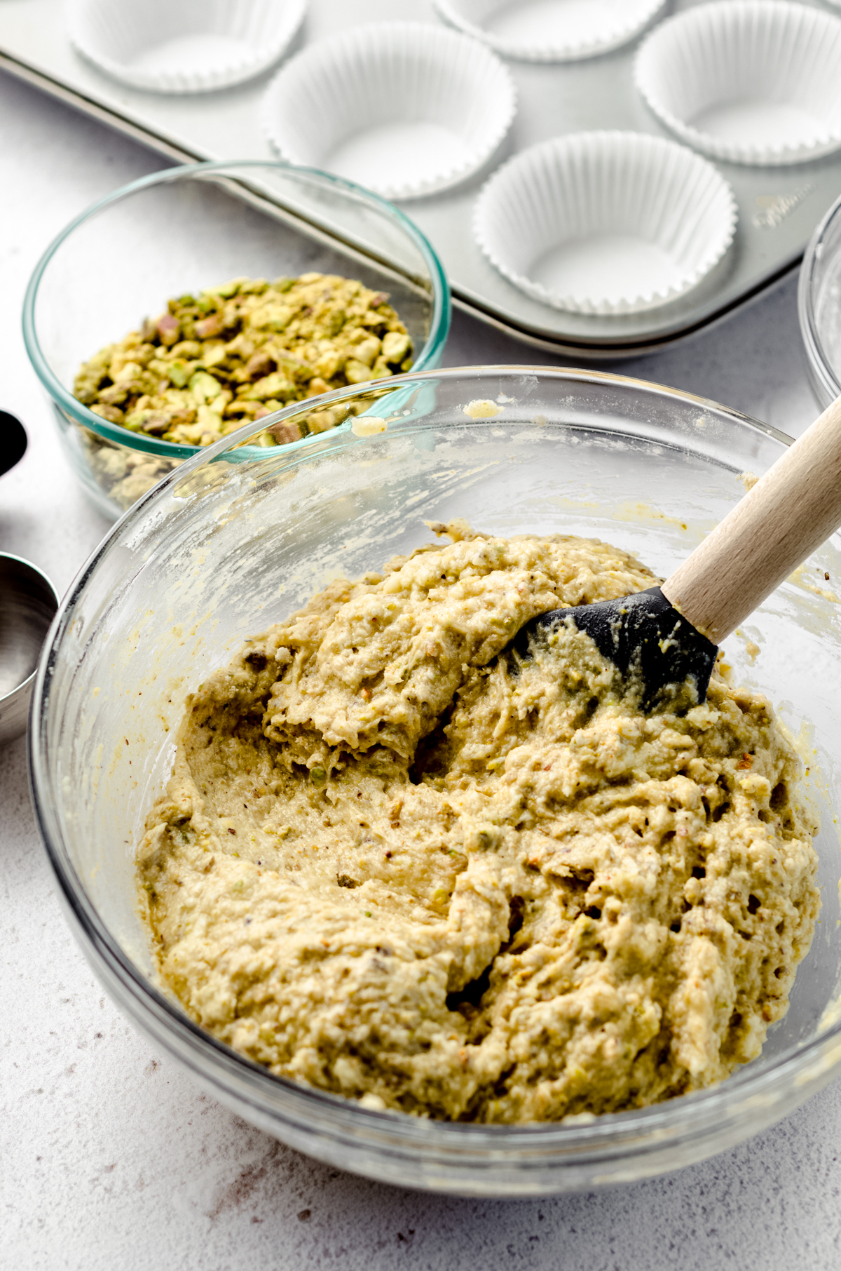 Pistachio muffin batter in a large glass bowl with a spatula.