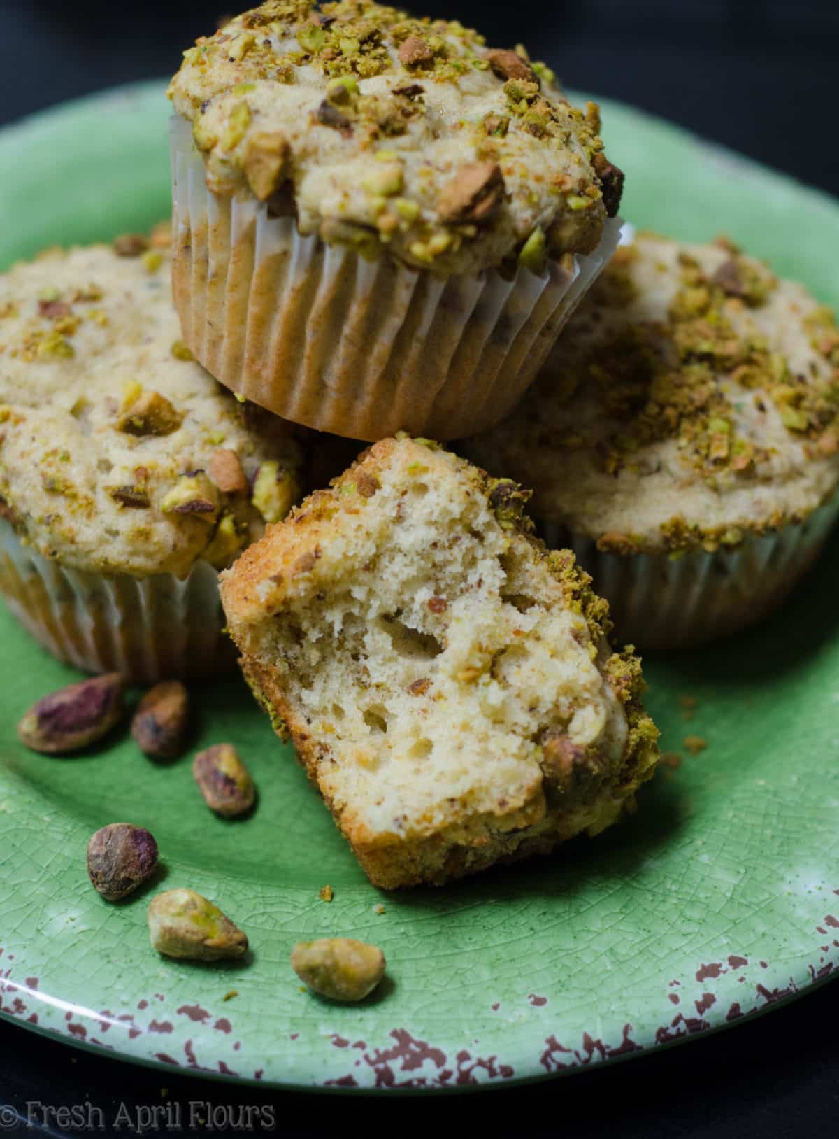 pistachio muffins on a plate and one has a bite taken out of it