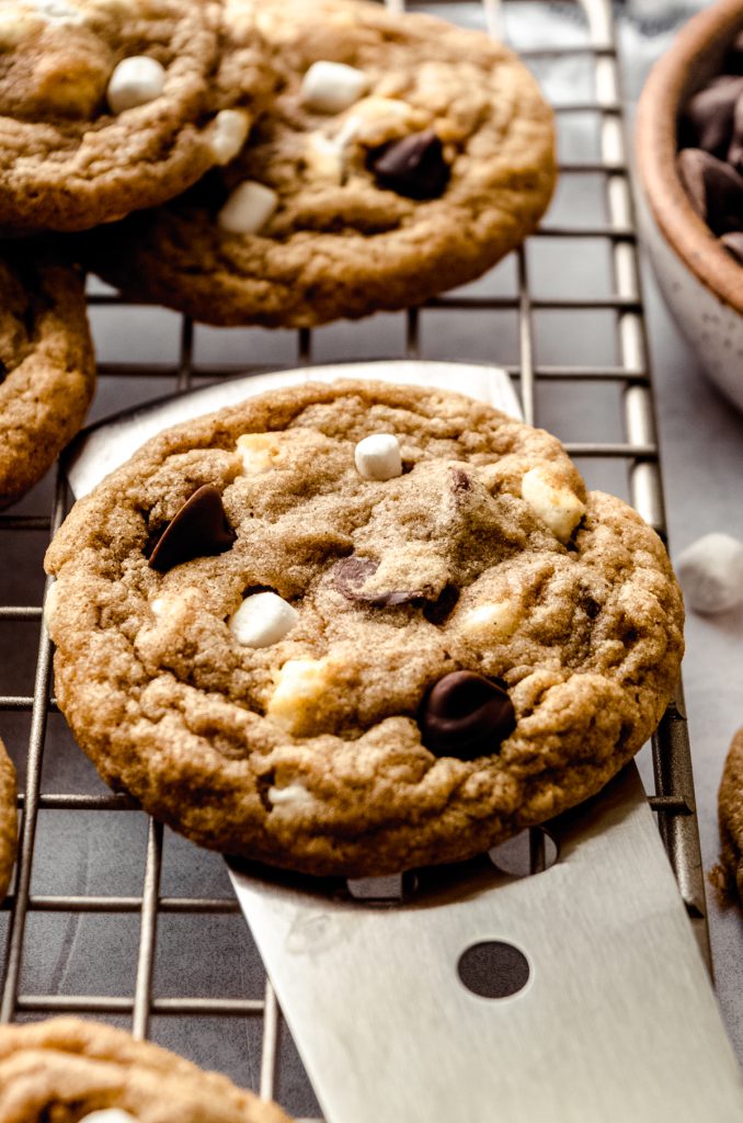 Someone is using a spatula to lift a s'mores chocolate chip cookie off of a cooling rack.