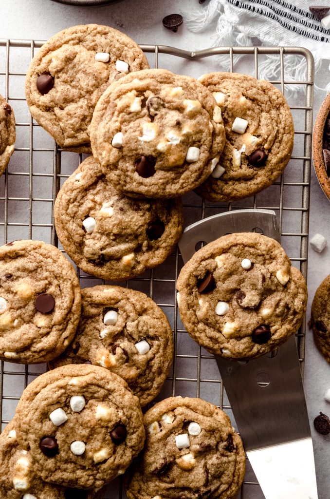 Aerial photo of s'mores chocolate chip cookies on a wire cooling rack with a spatula lifting one of them.