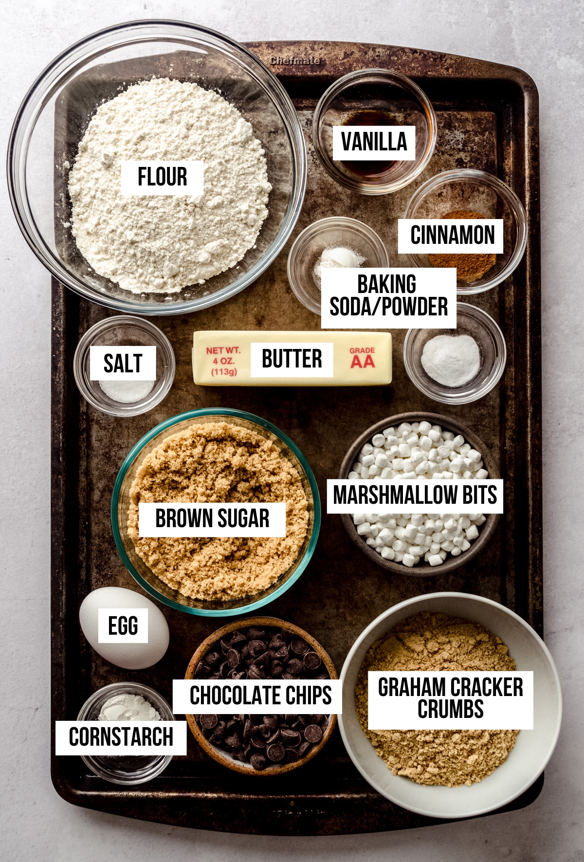 Aerial photo of ingredients to make s'mores chocolate chip cookies with text overlay labeling each ingredient.