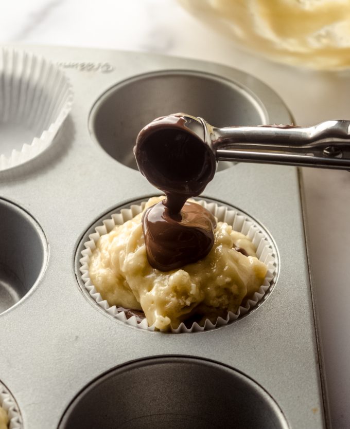 Someone is putting a dollop of Nutella onto muffin batter with a scoop.