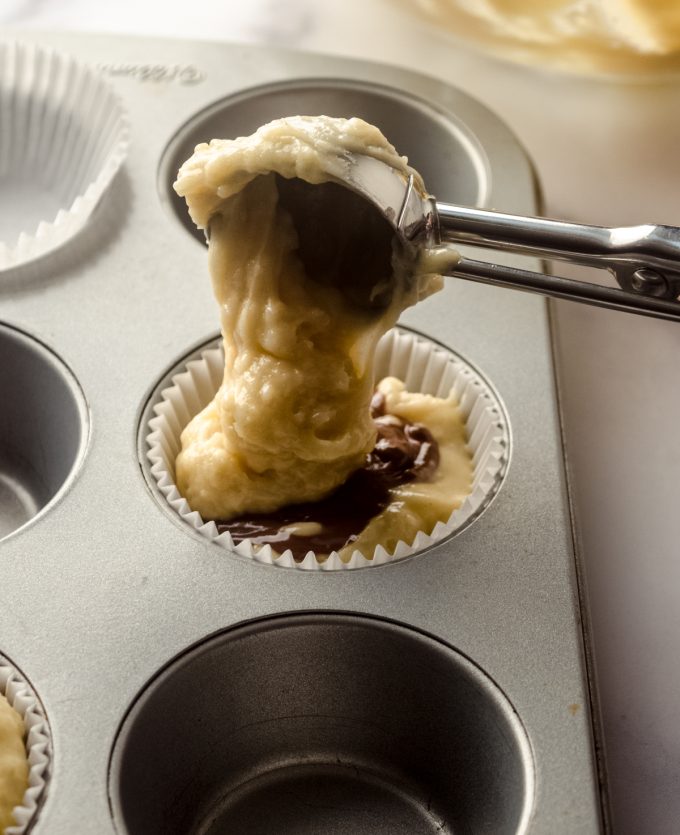 Someone is putting muffin batter into a pan with a scoop.