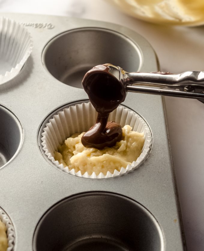 Someone is putting a dollop of Nutella onto muffin batter with a scoop.