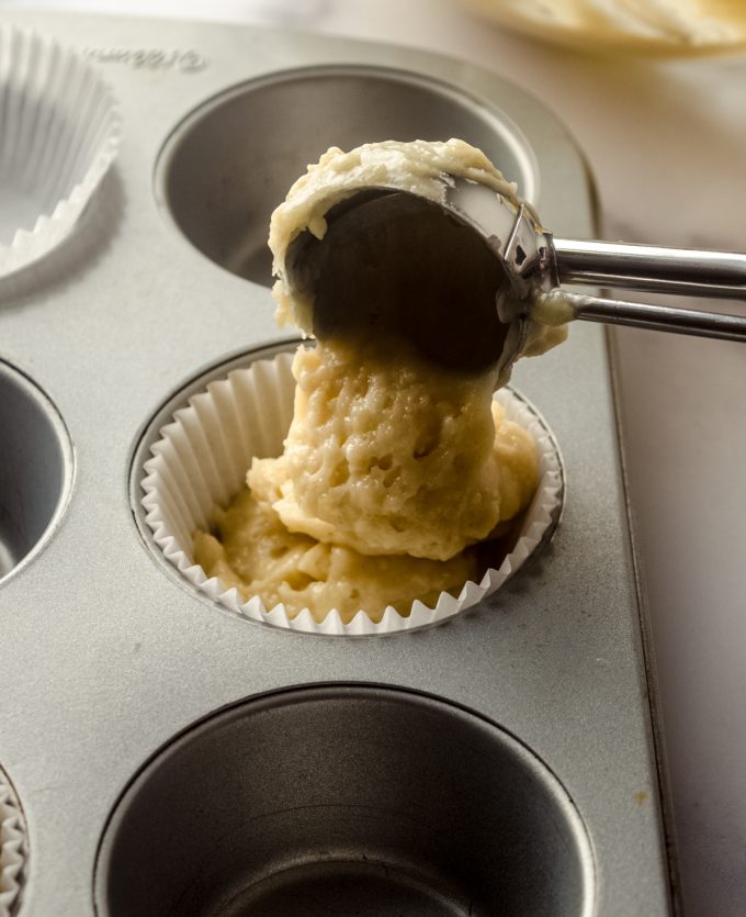 Someone is putting muffin batter into a pan with a scoop.