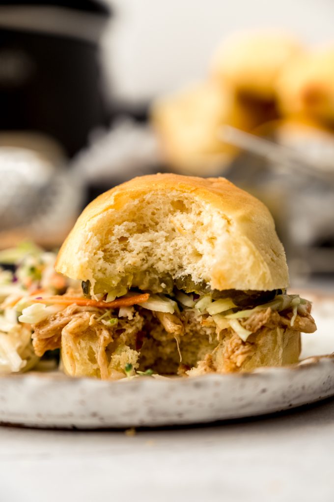 A shredded hot chicken sandwich on a plate with a bite taken out of it.