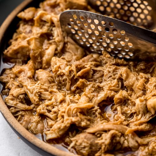 A bowl of shredded hot chicken with tongs in it.