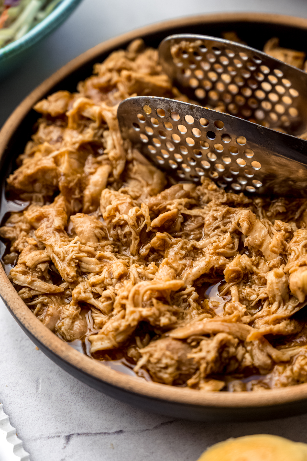 A bowl of shredded hot chicken with tongs in it.