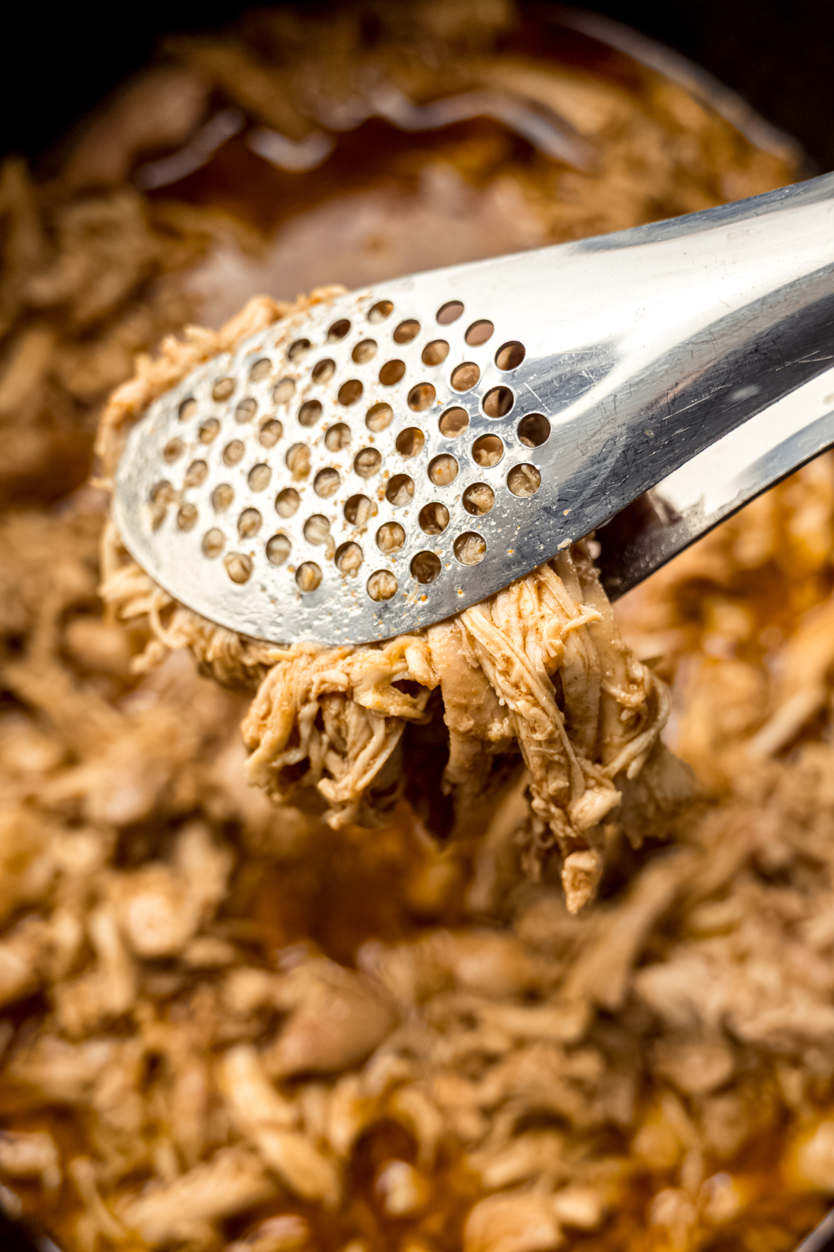 Tongs with shredded hot chicken in them.
