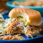 A hot chicken sandwich on a plate and the sandwich has a bite taken out of it.