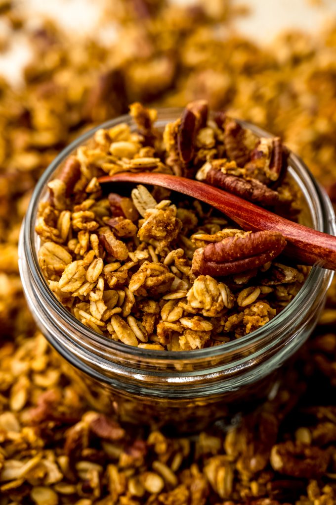 A jar of pumpkin granola with a wooden spoon in it.