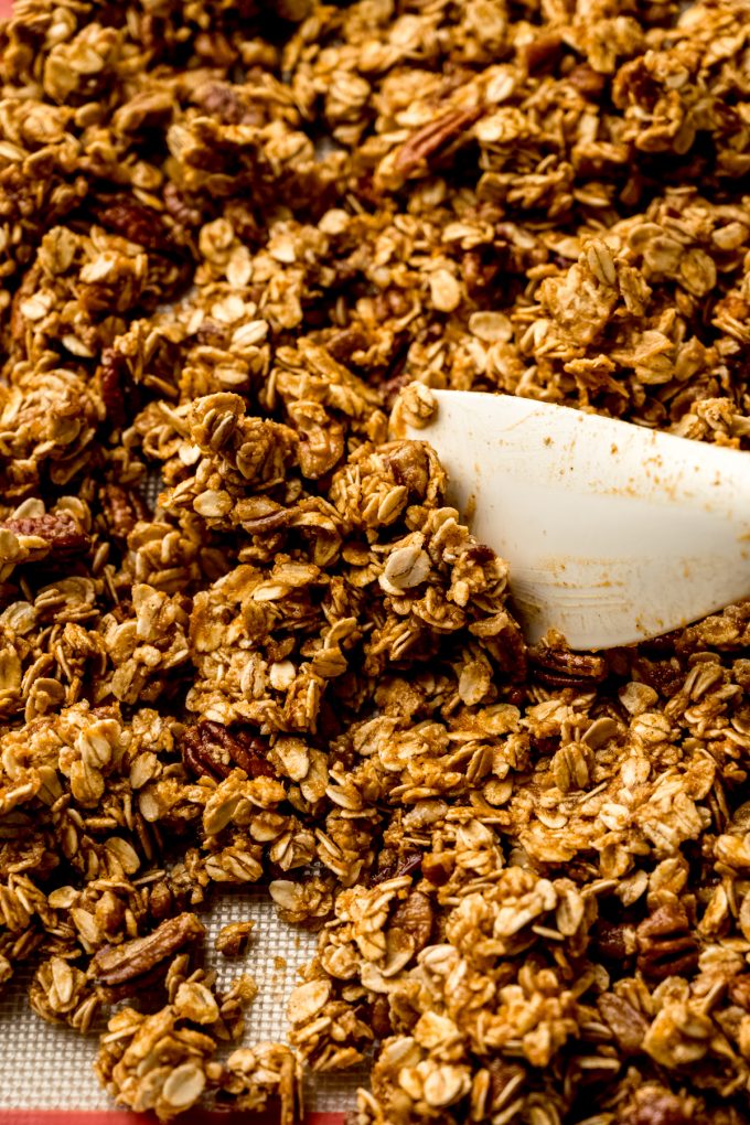A baking sheet of pumpkin granola ingredients getting stirred around with a spatula.