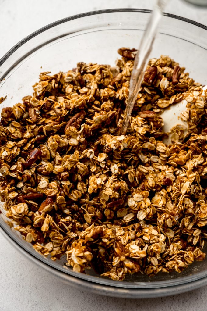 Someone os pouring melted coconut oil into a bowl of pumpkin granola.
