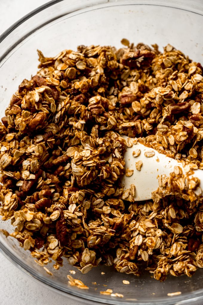 A bowl of pumpkin granola ingredients getting stirred together with a spatula.